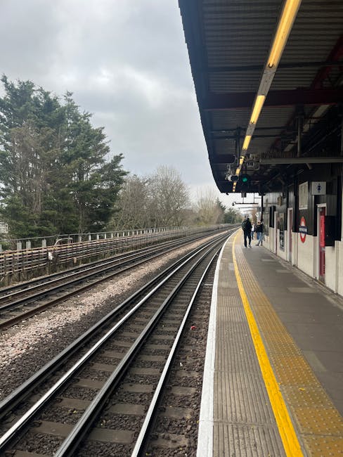A view of Ickenham railway station platform at night, showing the empty edge with tactile paving and yellow safety lines along the platform border. The station is illuminated by overhead lighting fixt