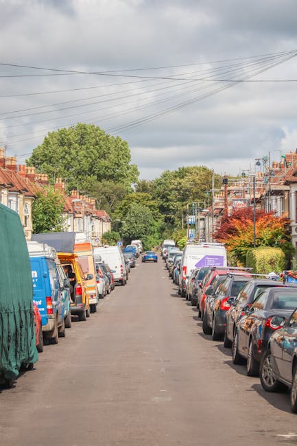 The image shows a narrow residential street in Ickenham during daytime with overcast weather. On both sides of the street, there are terraced houses with brick exteriors, chimneys, and small front gar